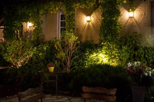 Warm exterior wall lights illuminating a home facade and planted garden borders at night